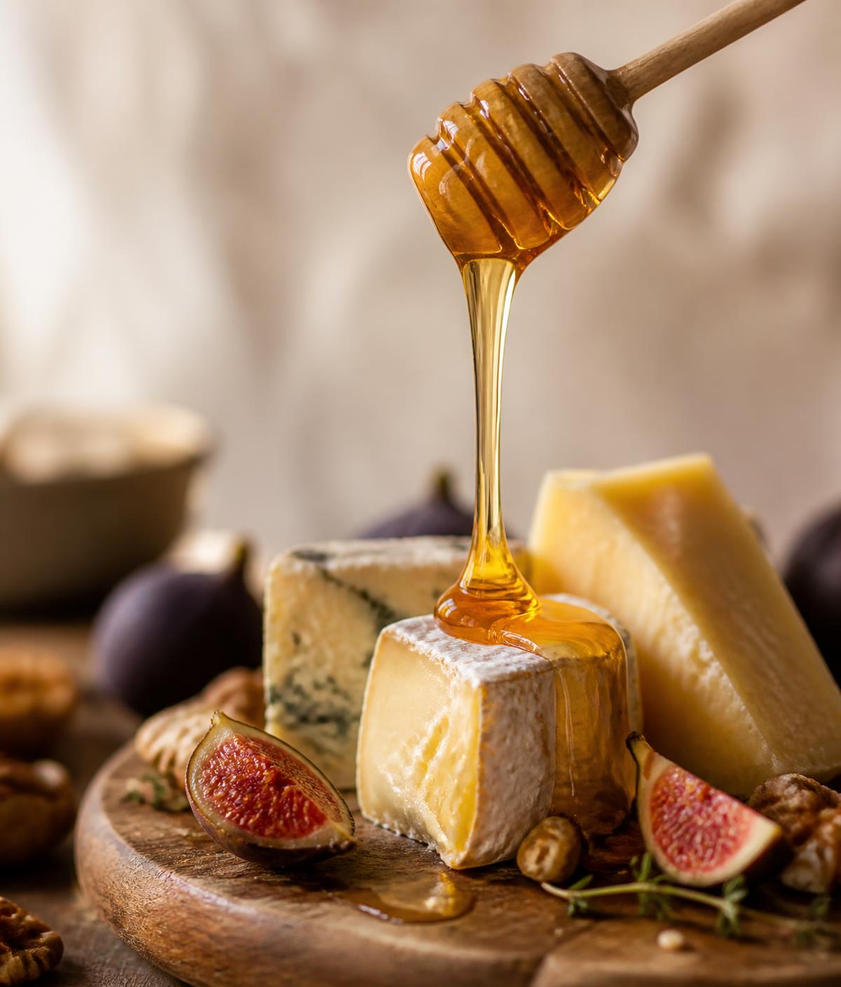 Golden raw honey drizzling from a wooden dipper over a cheese and fig board